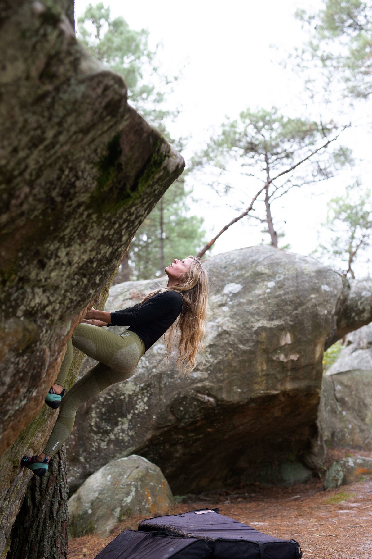 Claire Louise Foster bouldering on a mossy rock in a pine forest